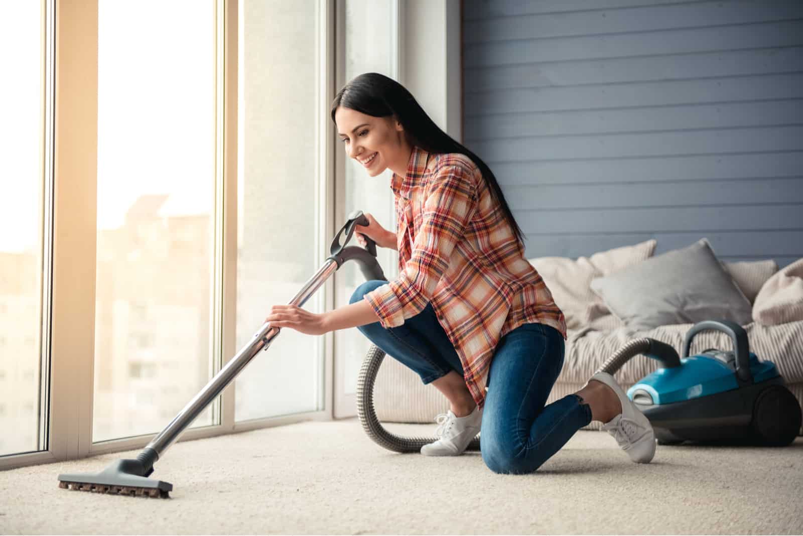 Beautiful young woman is smiling and using a vacuum cleaner while cleaning floor at home