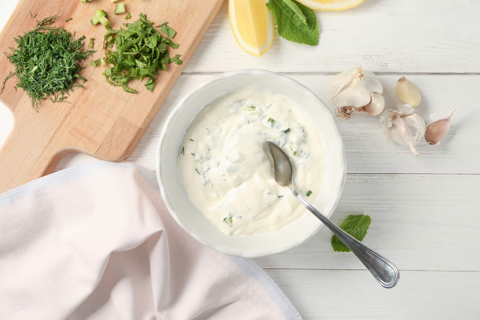 Delicious yogurt sauce in bowl with ingredients on wooden background