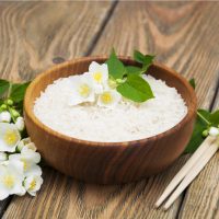 Wooden plate with jasmine rice and jasmine flowers on a wooden background