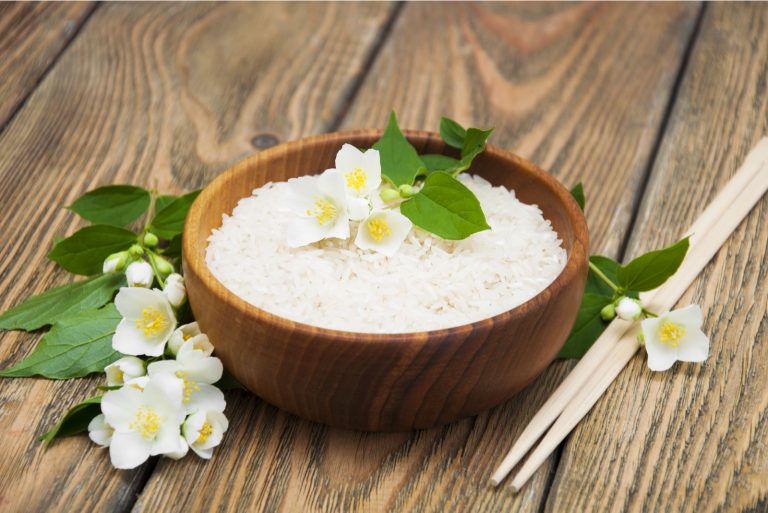 Wooden plate with jasmine rice and jasmine flowers on a wooden background