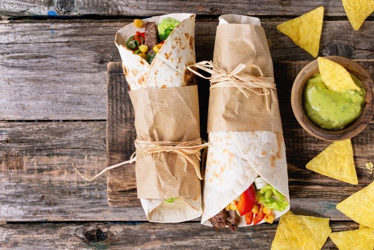 two tortilla wrap and corn chips with avocado dip placed on the wooden platter