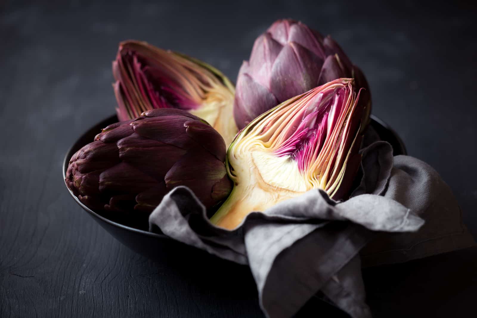 Fresh ripe artichokes in a bowl against black wooden background
