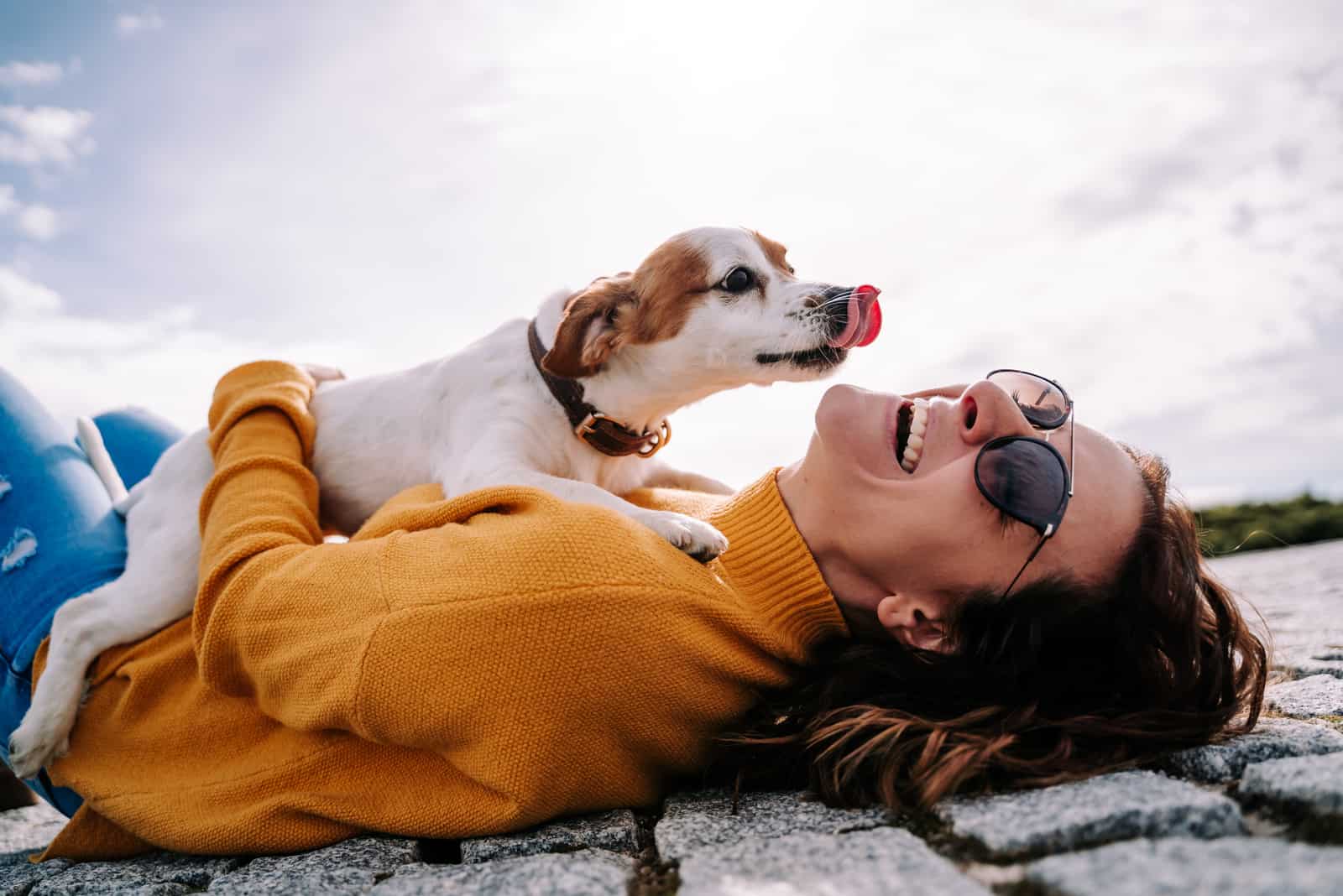 A beautiful woman laughing while her pet is licking her face
