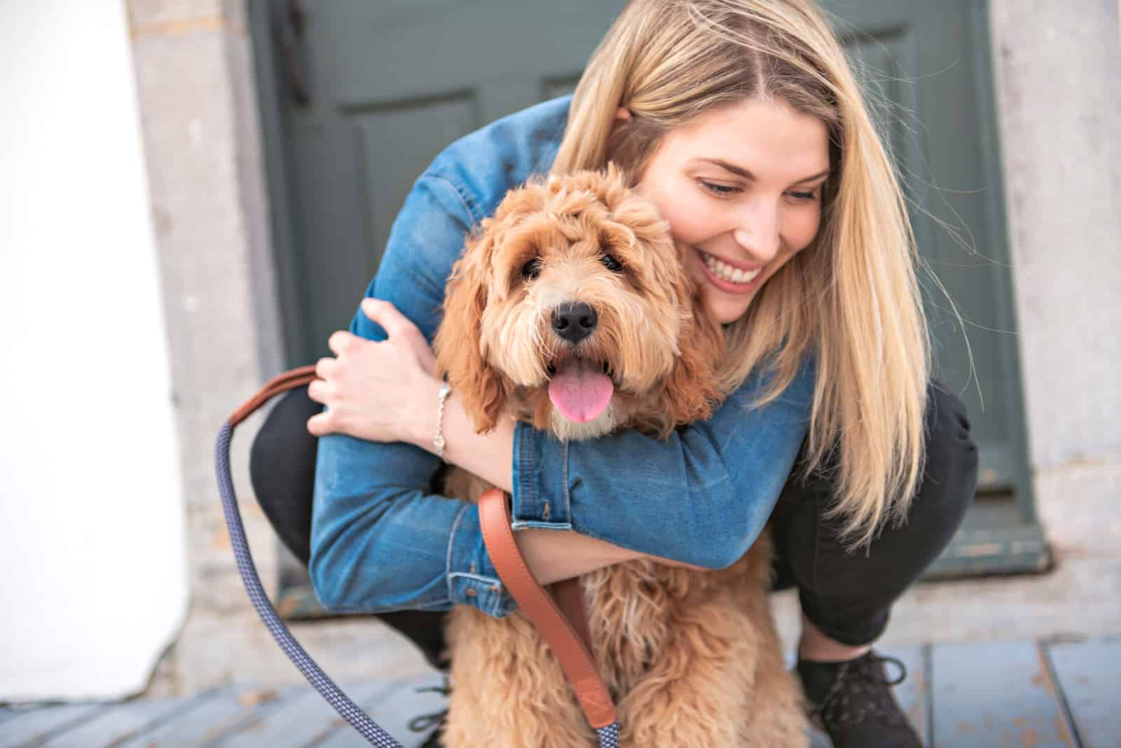 a smiling blonde hugs a labradoodle outside