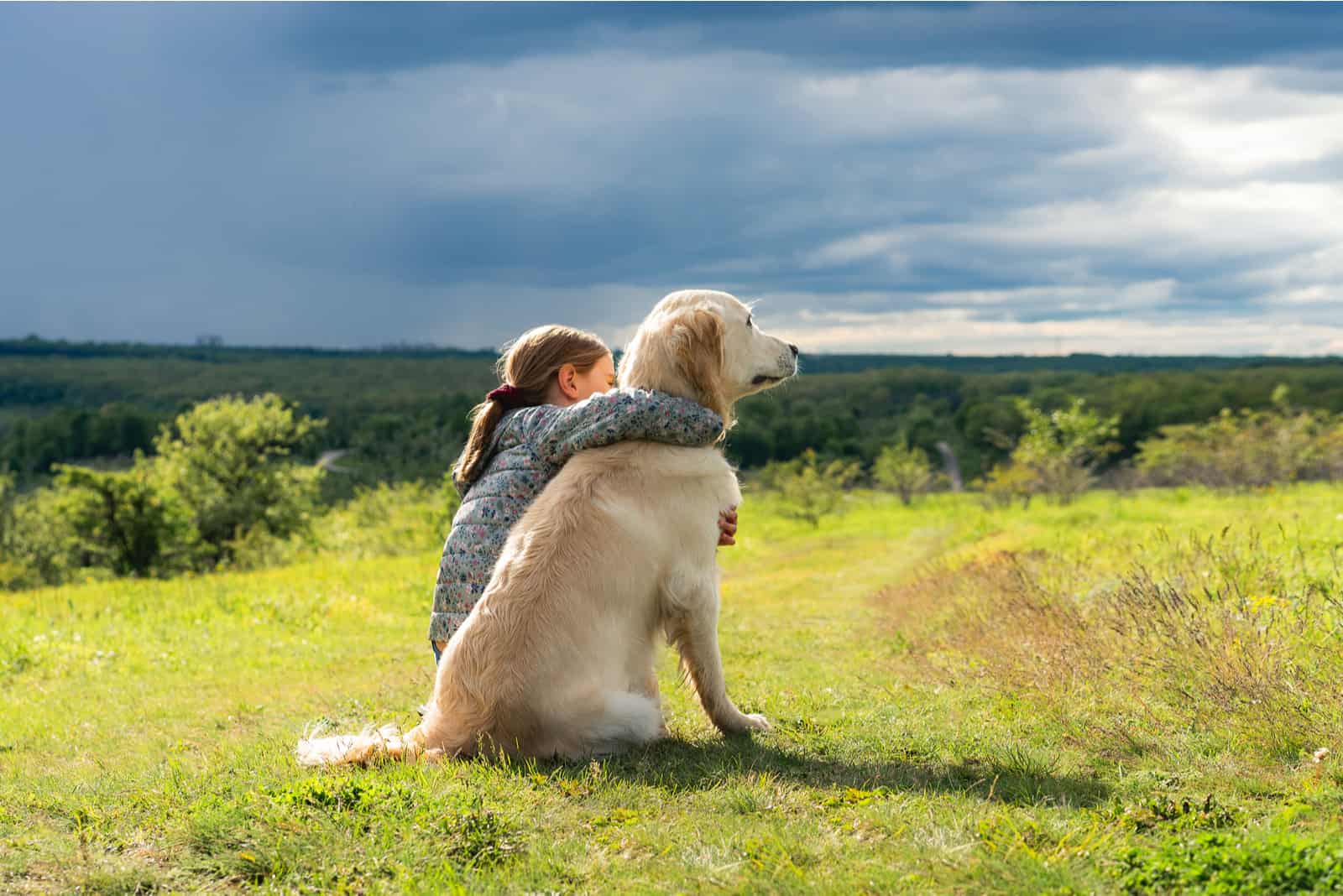 beautiful little girl hugging loyal dog in nature