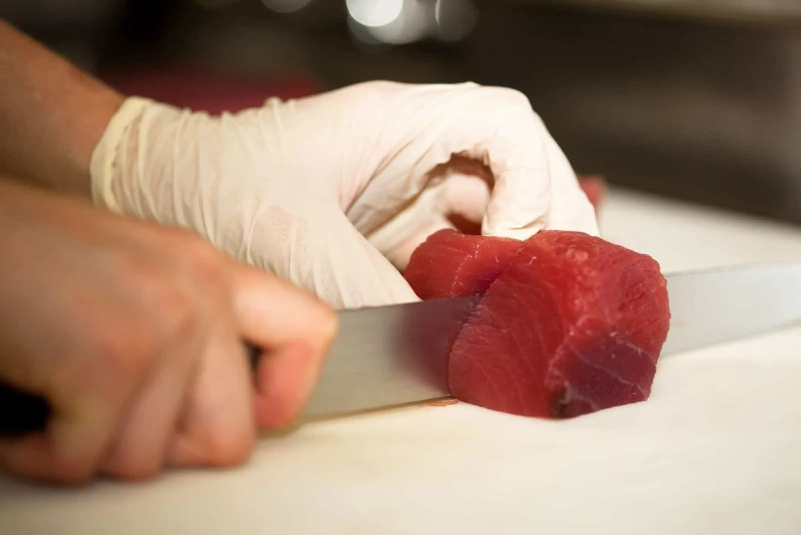 chef cutting raw tuna on top of cutting board in focus