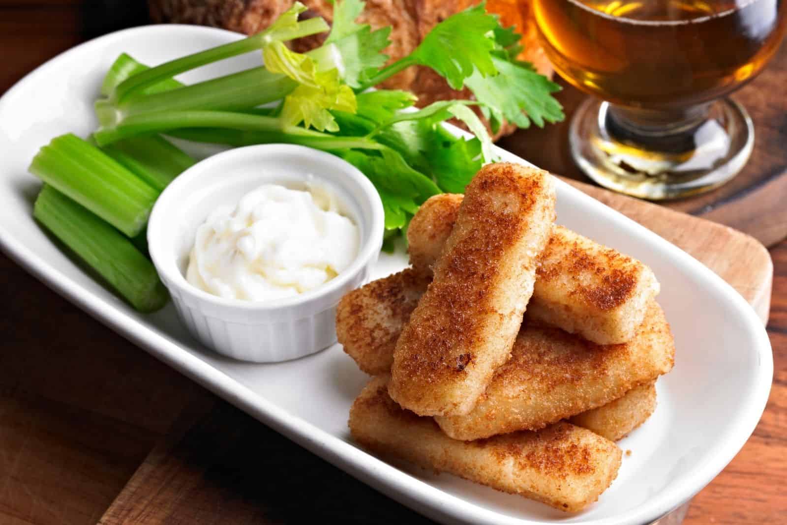 fish sticks with celery and mayo on plate with wine