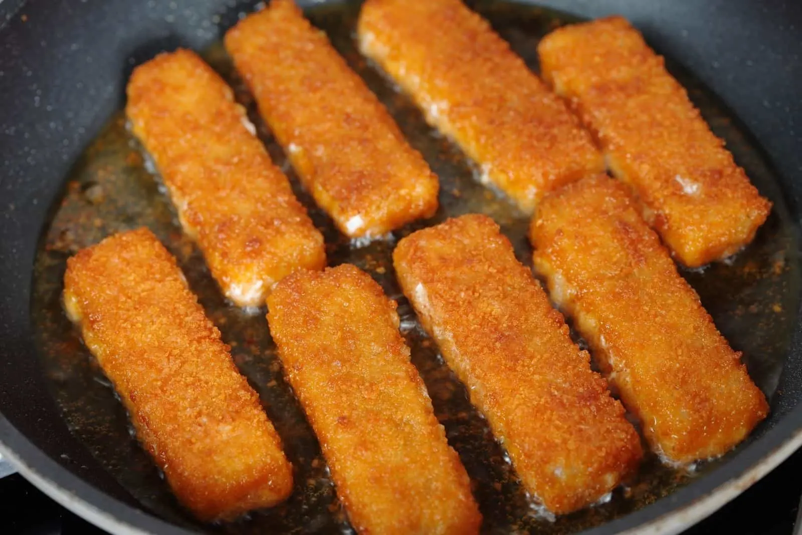 fried fish sticks in hot cooking oil in pan