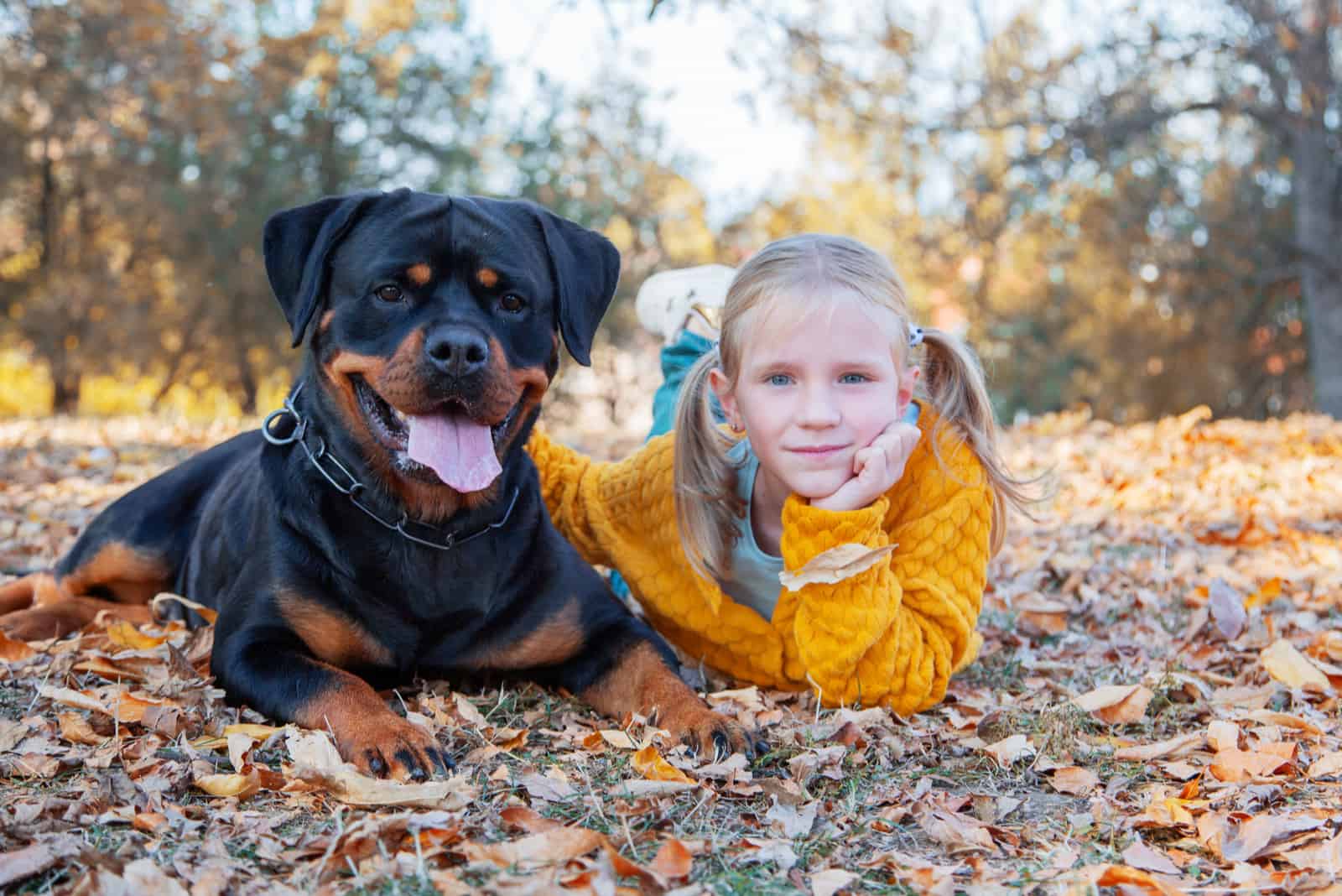 cute blonde girl and her Rottweiler dog lying on leaves