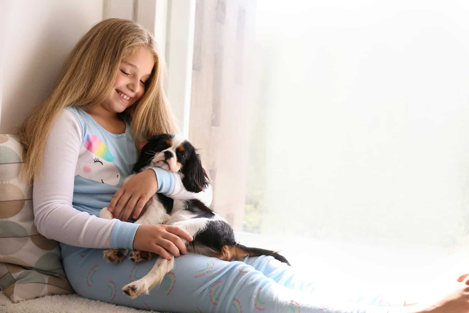girl with long blonde straight hair playing with black and white Cavalier King Charles Spaniel