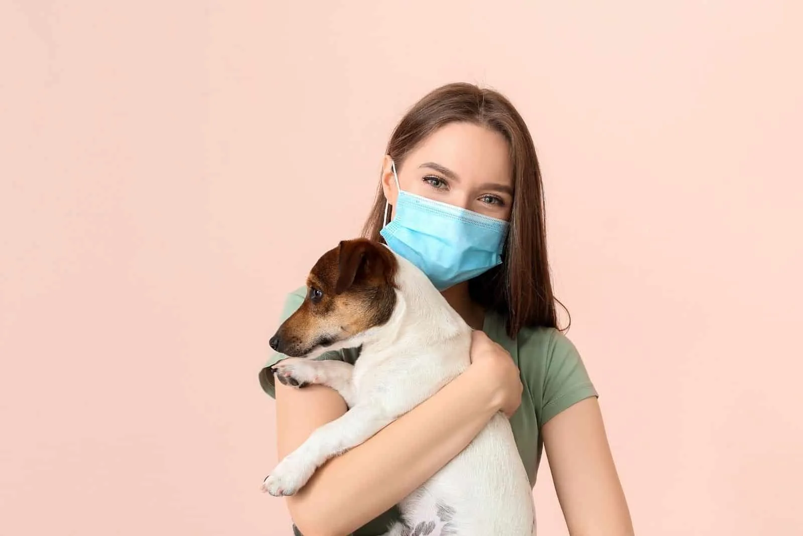 woman with a face mask hugging a dog in pink background 