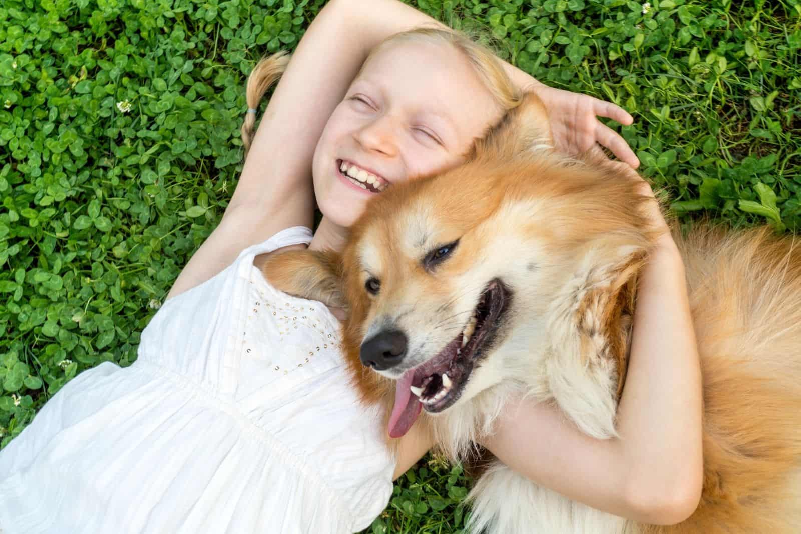 golden corgi hugged by a girl lying down on green grass