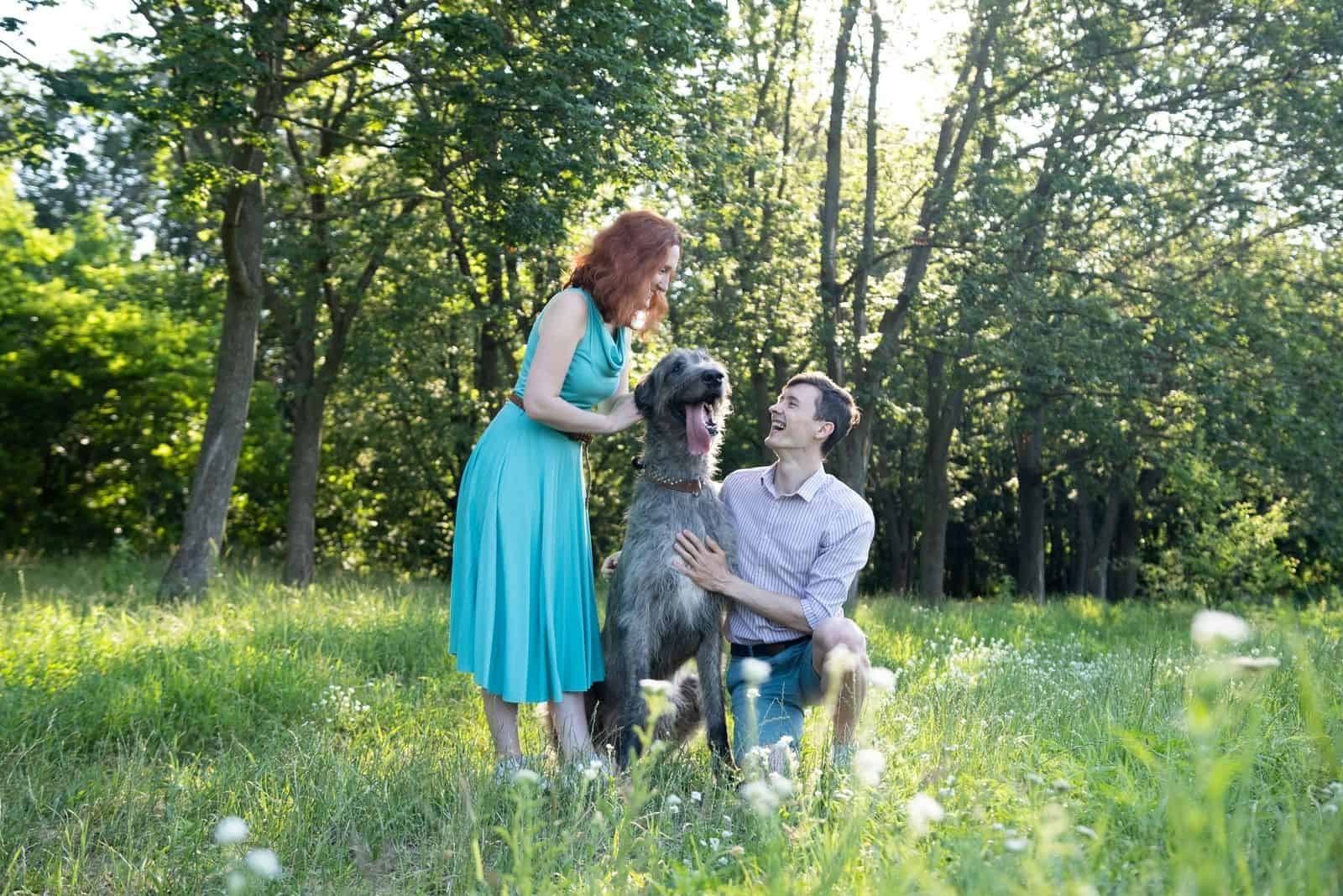 man and woman caressing a tall irish wolfhound in the forest