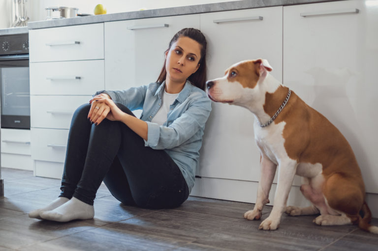 sad woman and dog sitting in kitchen on floor