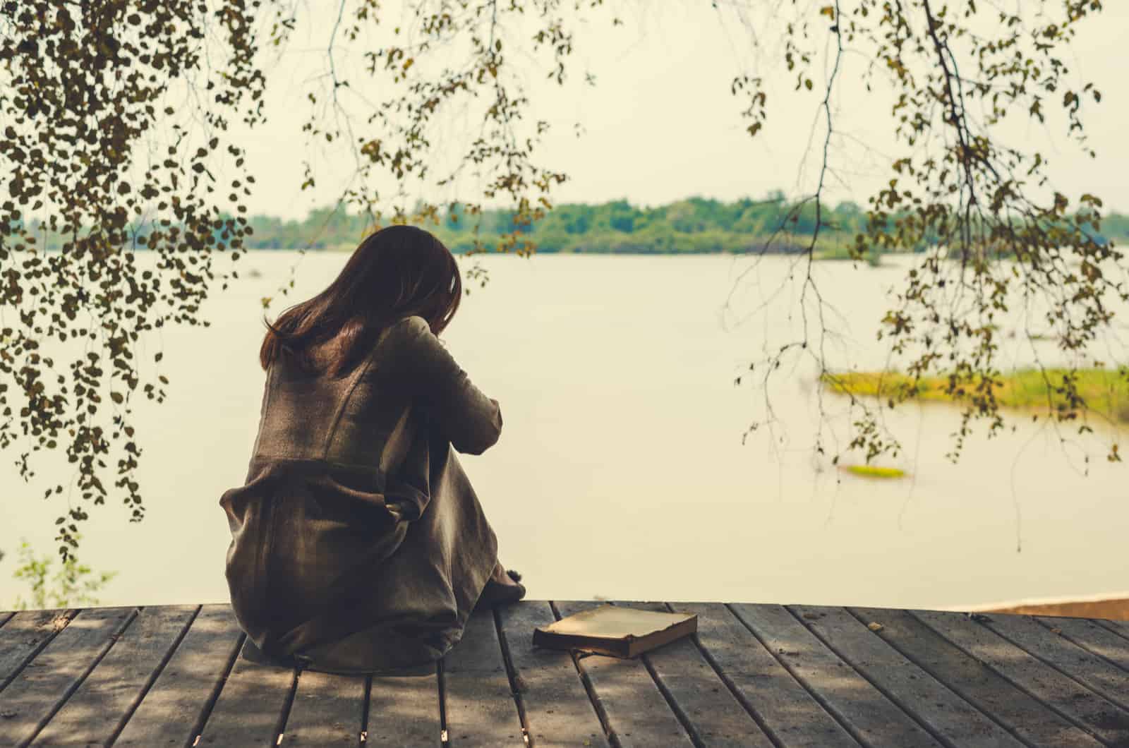 sad woman sitting on dock by lake