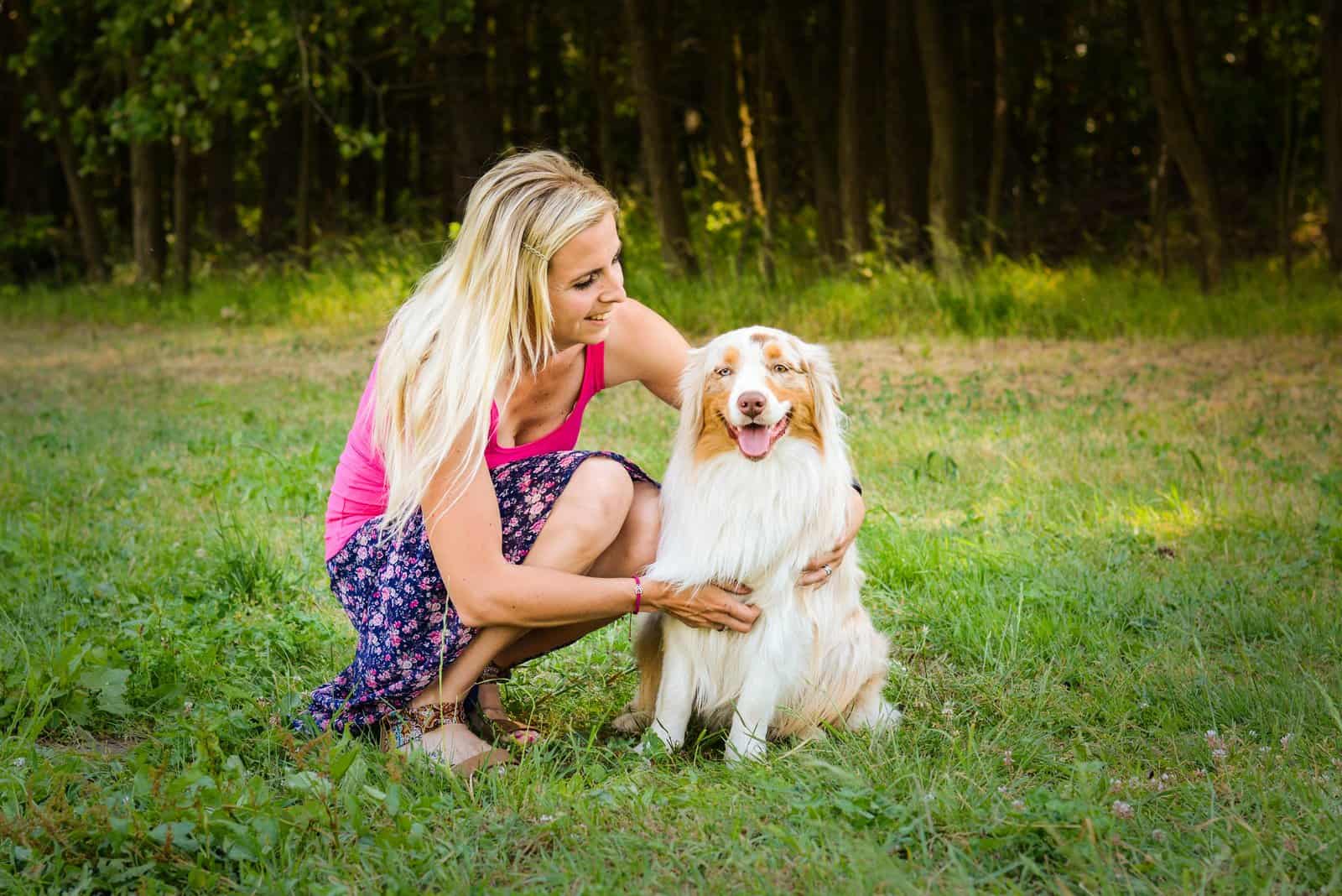 a woman is playing on the grass with an Austrian shepherd