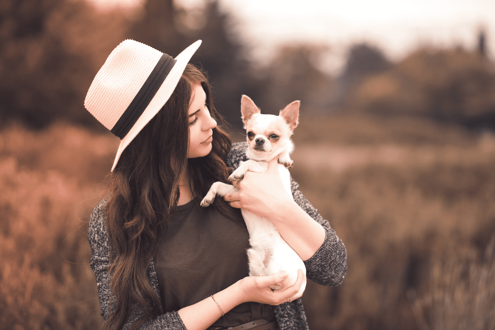 a beautiful woman with a hat on her head holds a chihuahua in her arms