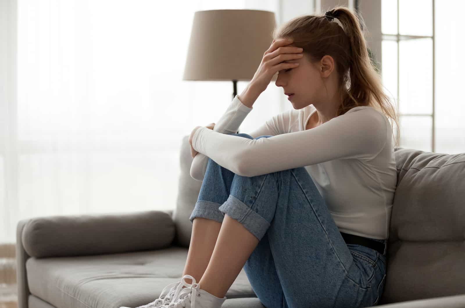 sad woman sitting curled up on sofa