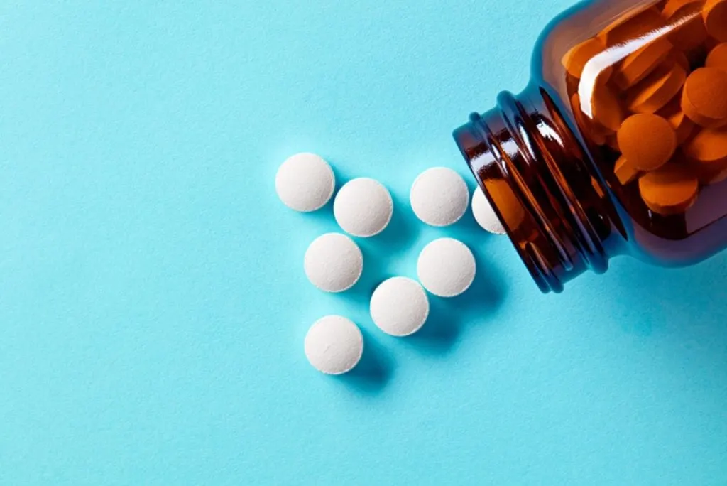White medical pills and tablets spilling out of a drug bottle