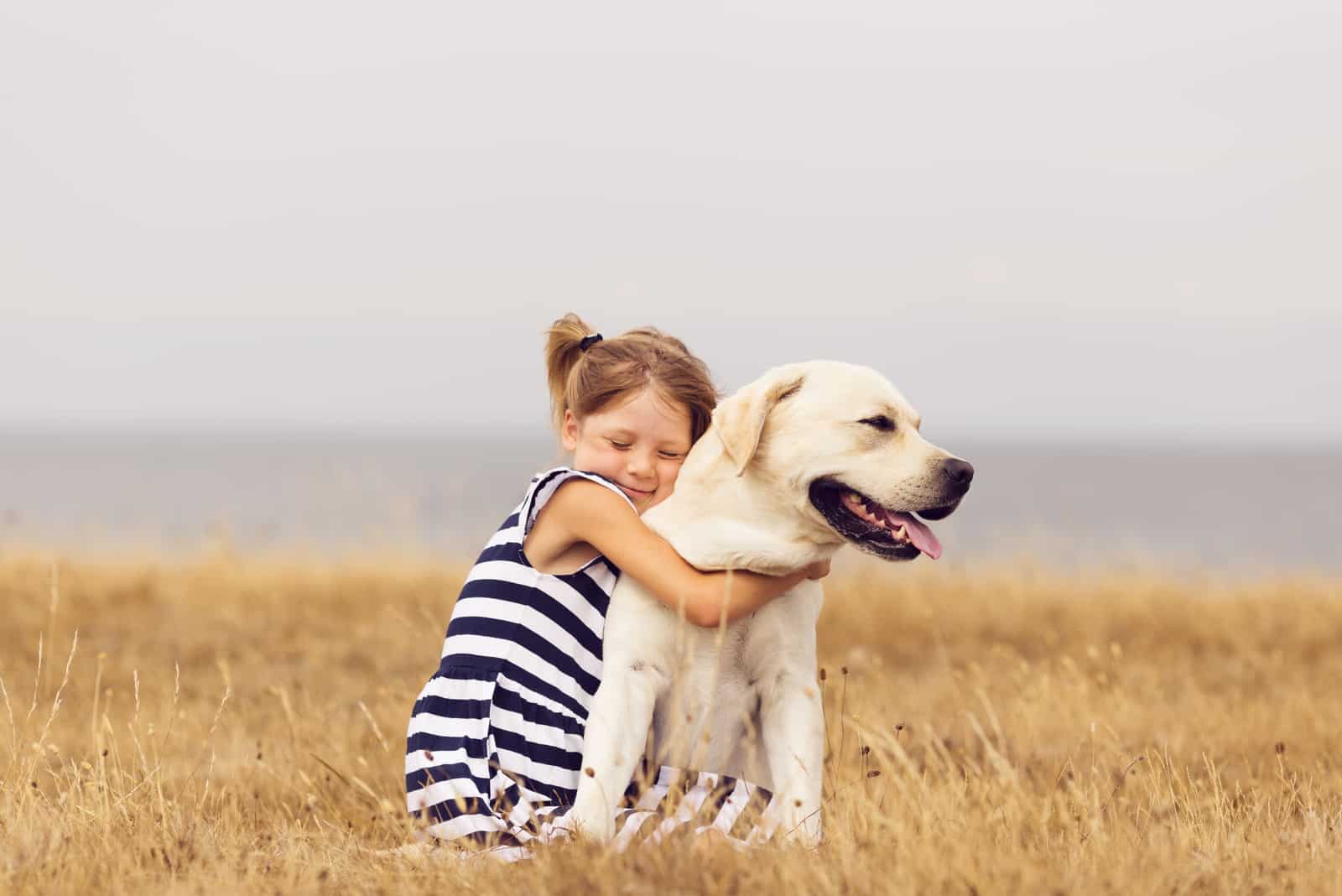 little girl hugging a labrador retriever