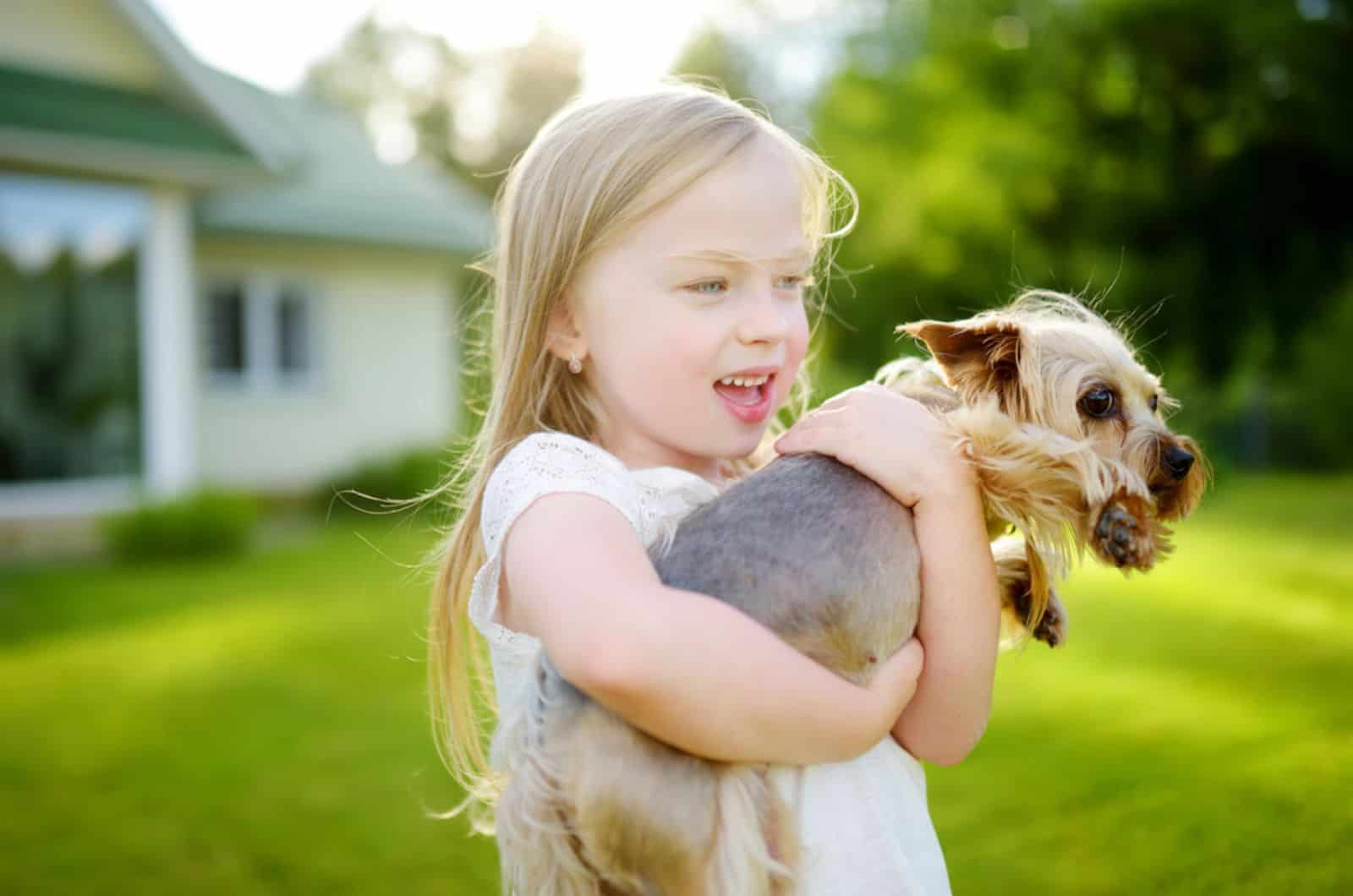 a little girl holding her yorkshire terrier dog in the yard