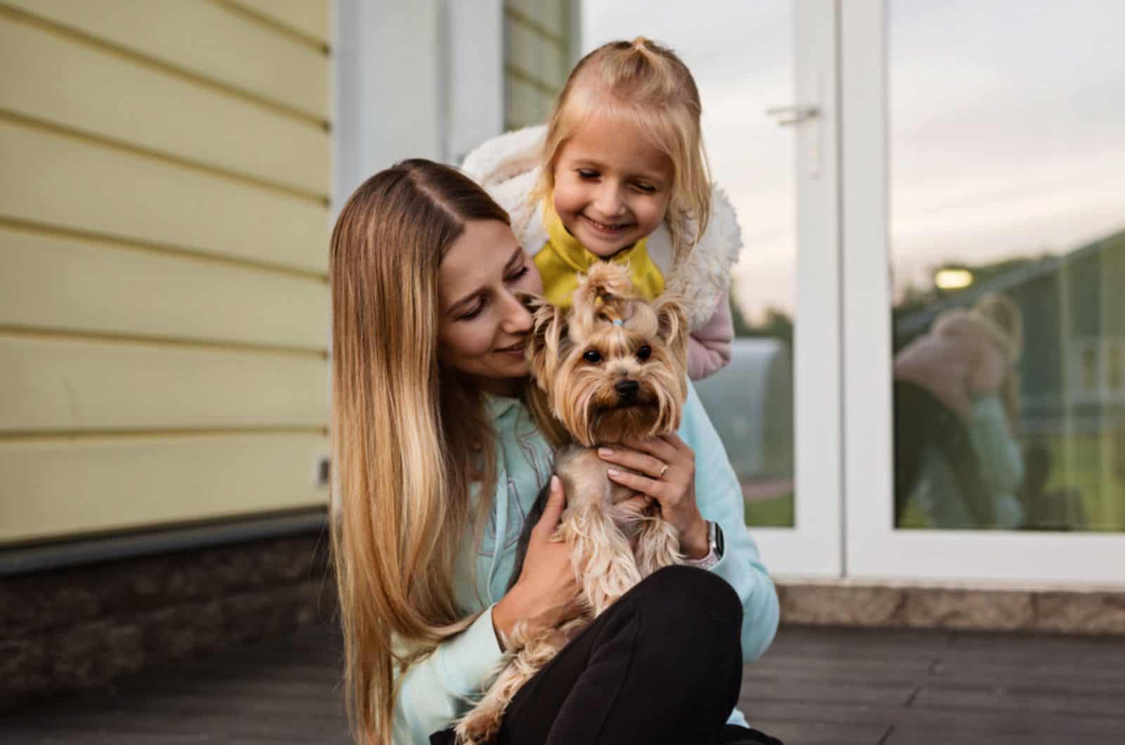 woman holding small dog yorkshire terrier next sitting little girl