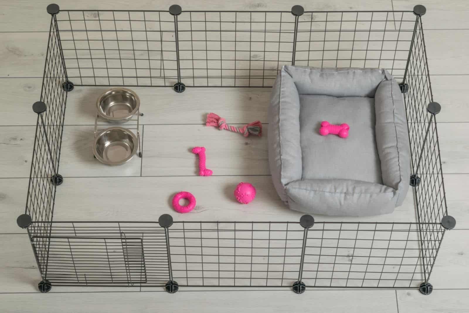 A home aviary for a dog with toys, a bowl and a bed