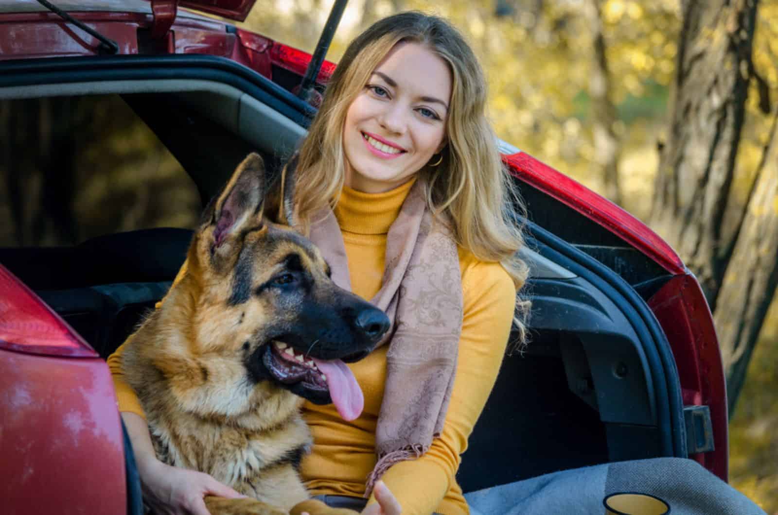 a girl and her dog german shepherd sitting on the car trunk