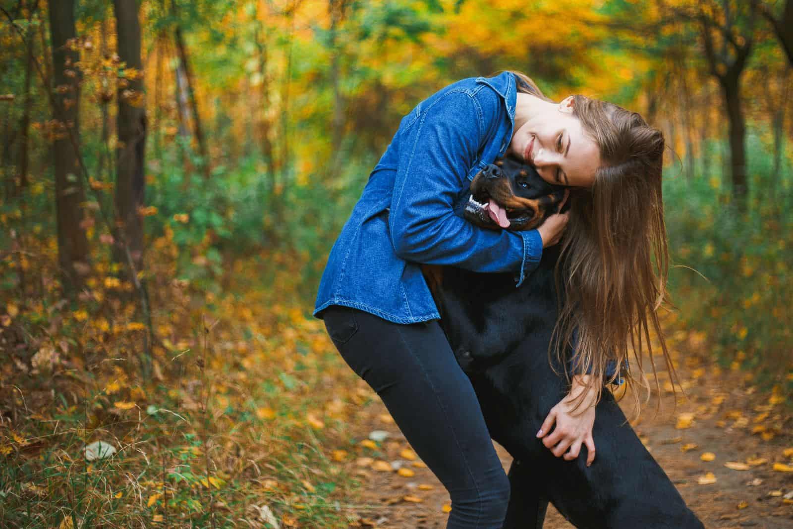 a woman with a Rottweiler cuddling in the forest