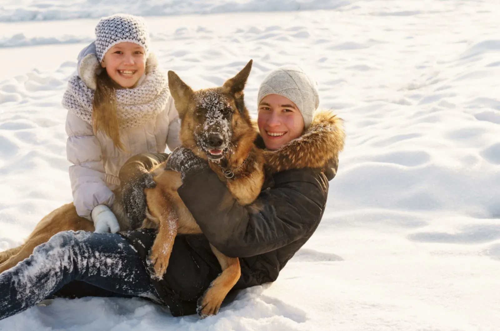 joyful teens playing with their german shepherd in the snow