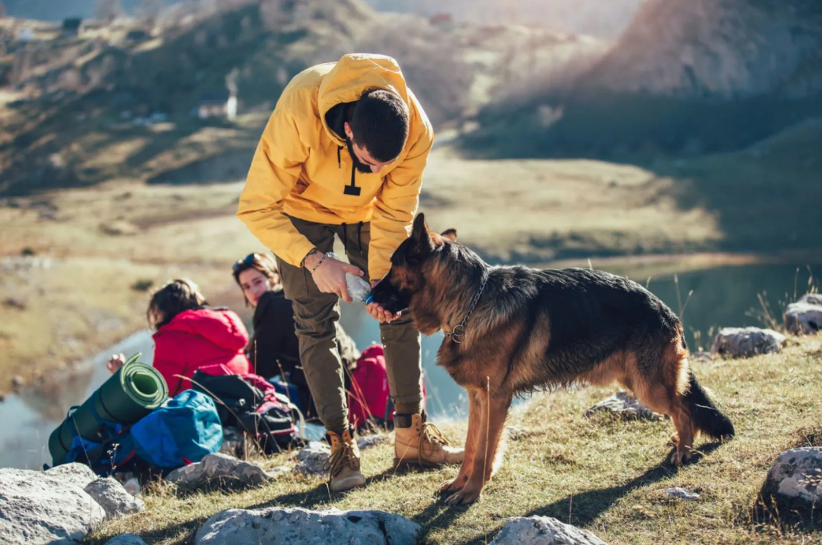 man gives water to the dog while resting from hiking