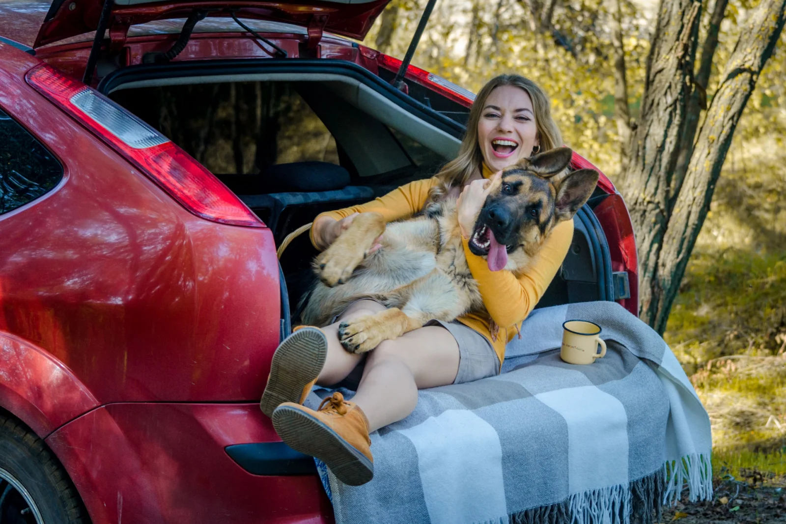 A happy Caucasian girl and a German shepherd lie in the trunk of a car in nature