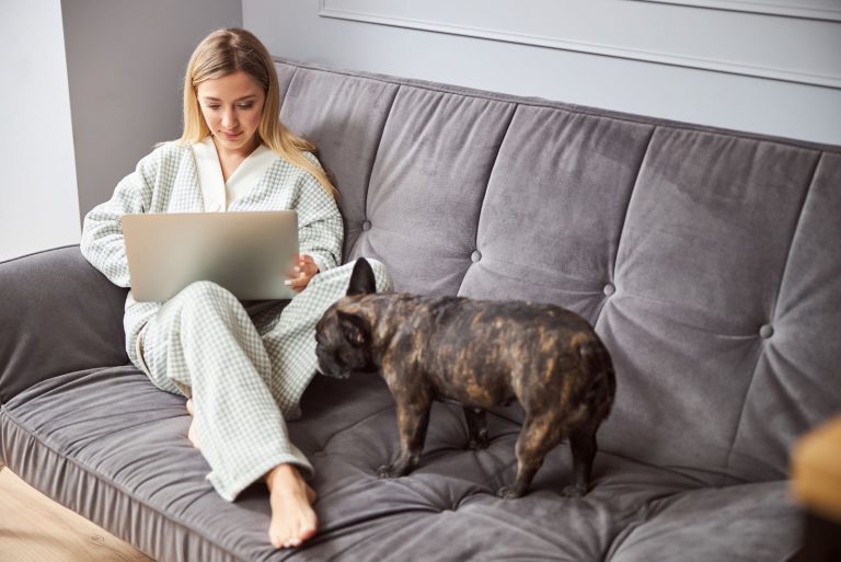 a woman is sitting on a couch, a dog is sniffing her feet