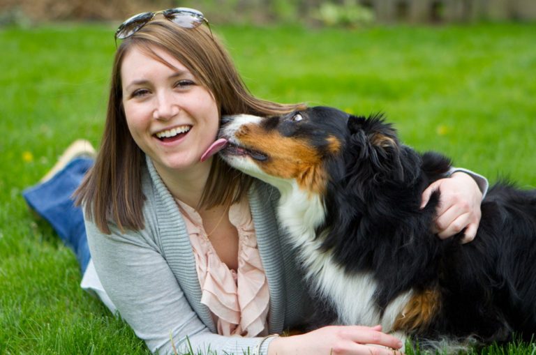 smiling women laying in the grass with her dog licking her face