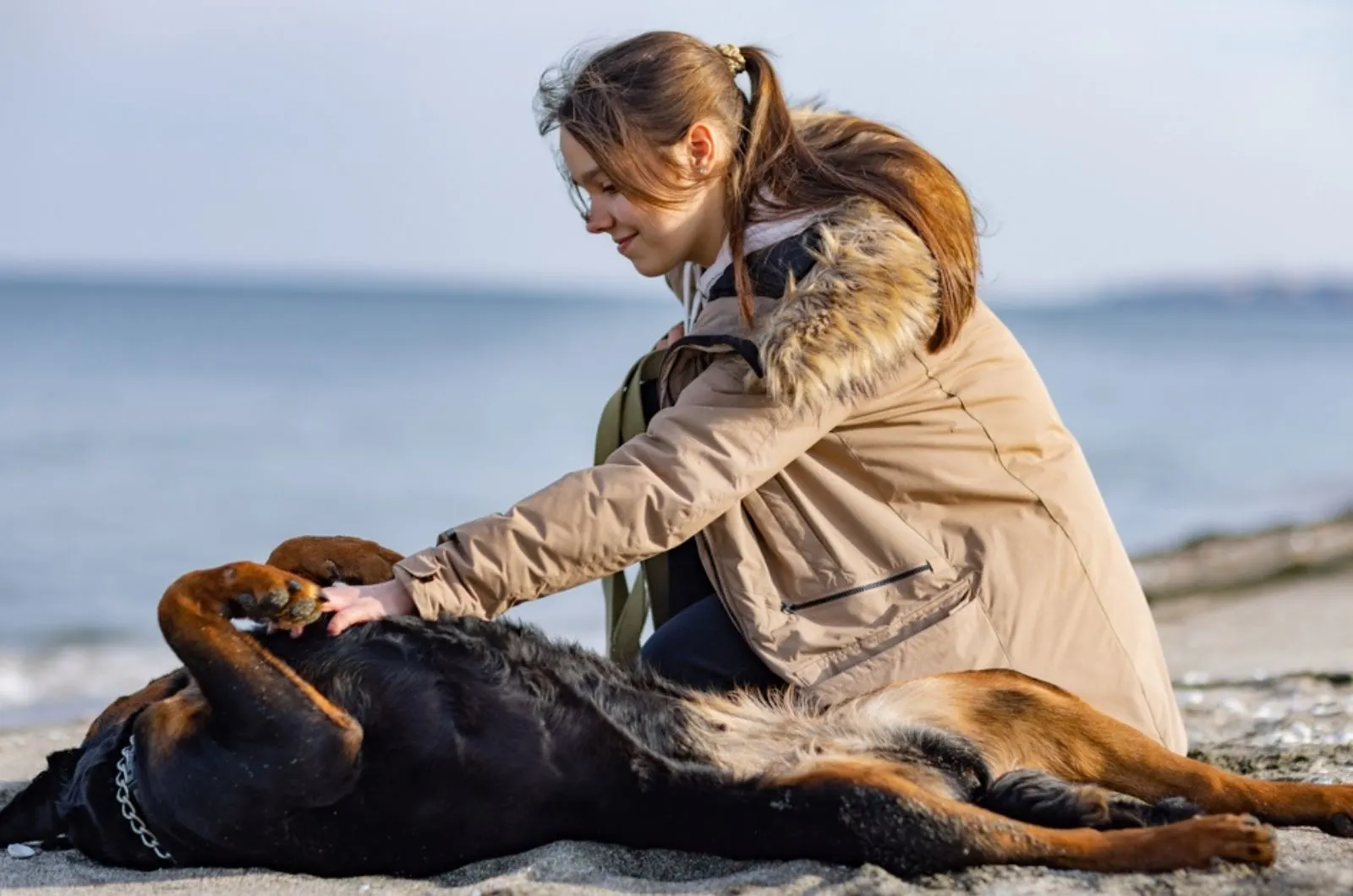 a girl cuddling her rottweiler on the beach