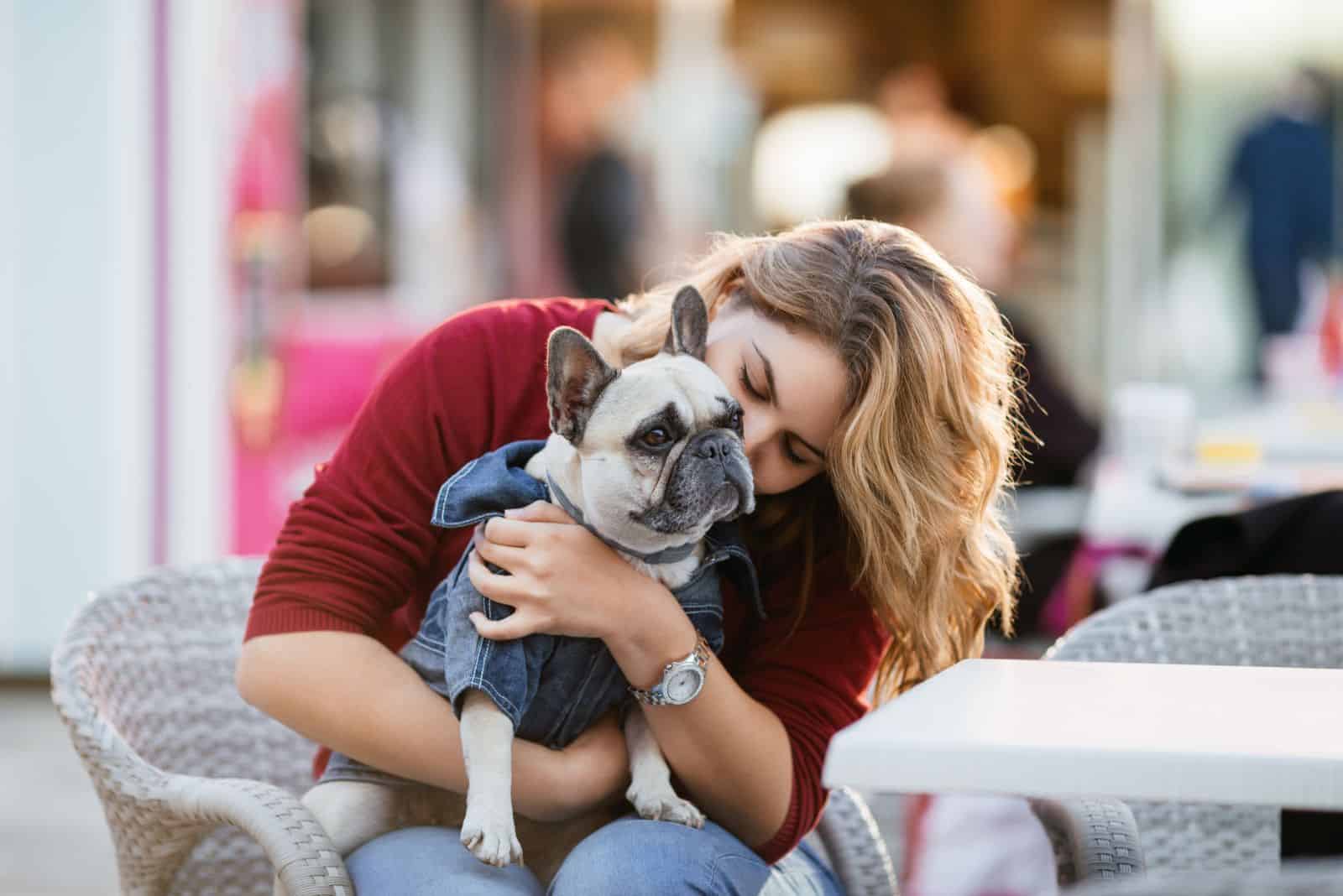 a woman holds a white French bulldog in her arms