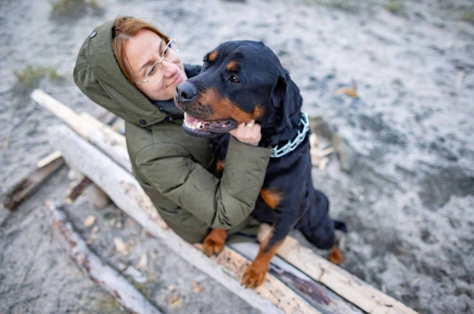 a woman hugging rottweiler dog on the bench