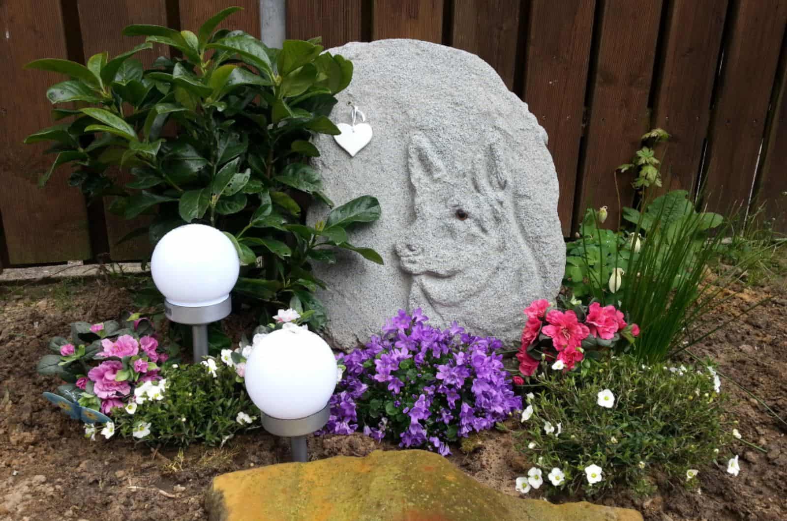 grave of a dog with artful tombstone in backyard