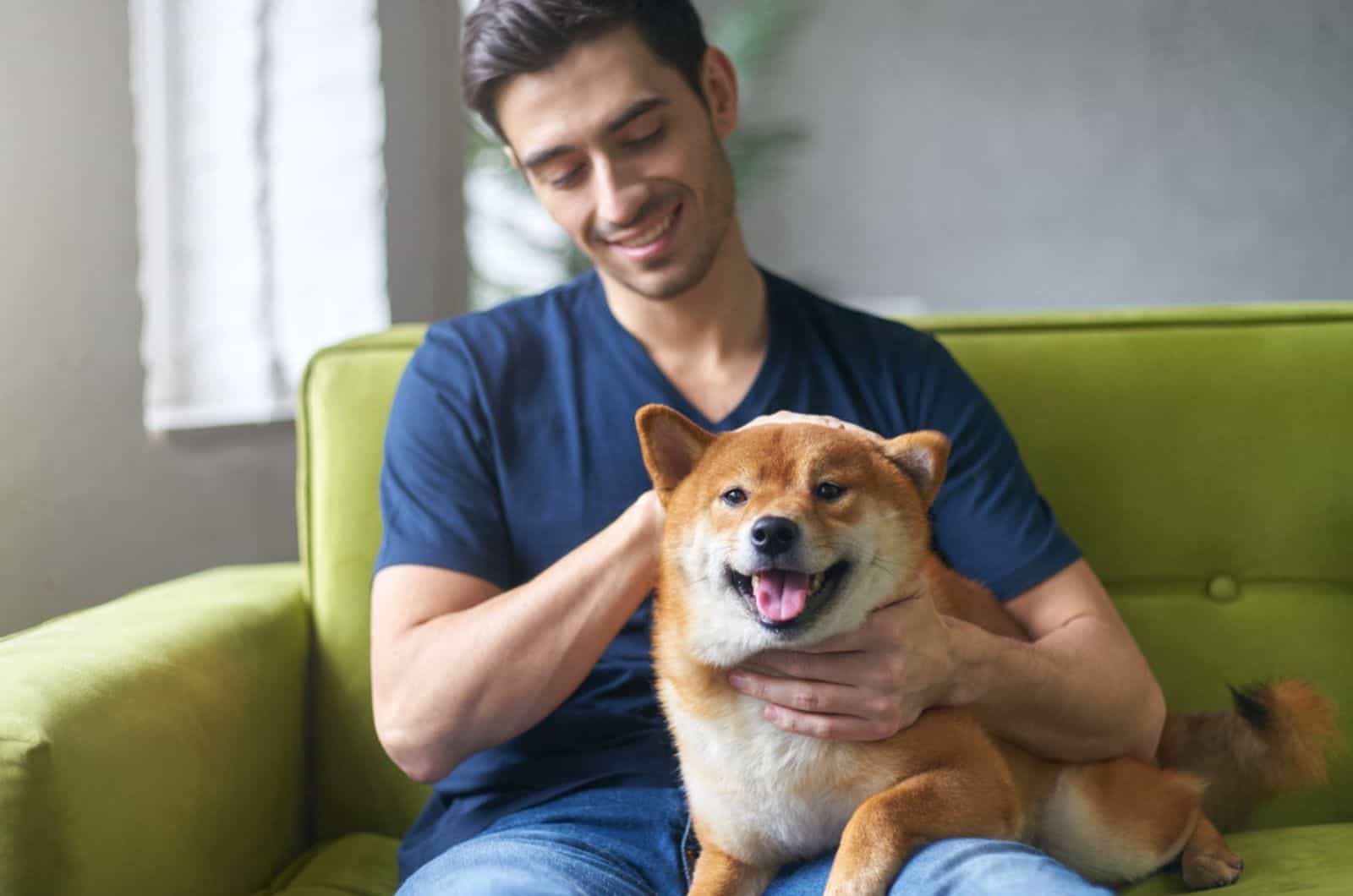 guy petting his dog shiba inu on the couch