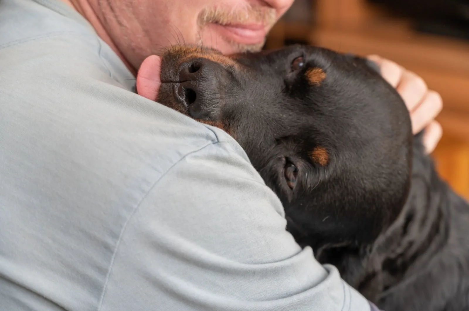 man cuddling rottweiler dog indoors