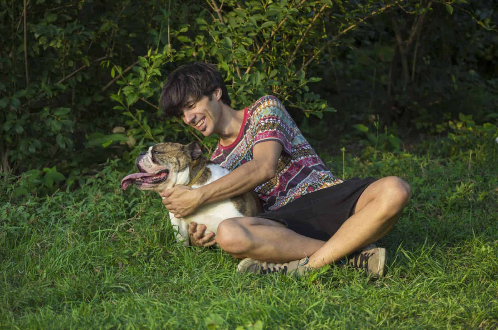 man hugging his bulldog in the grass