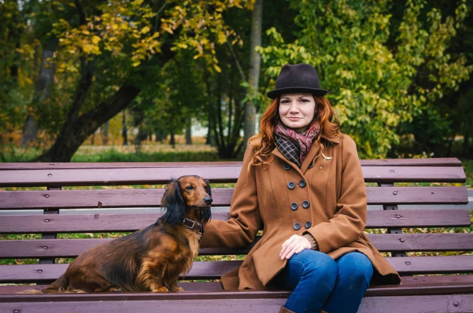 woman and dachshund dog sitting on the bench in the park