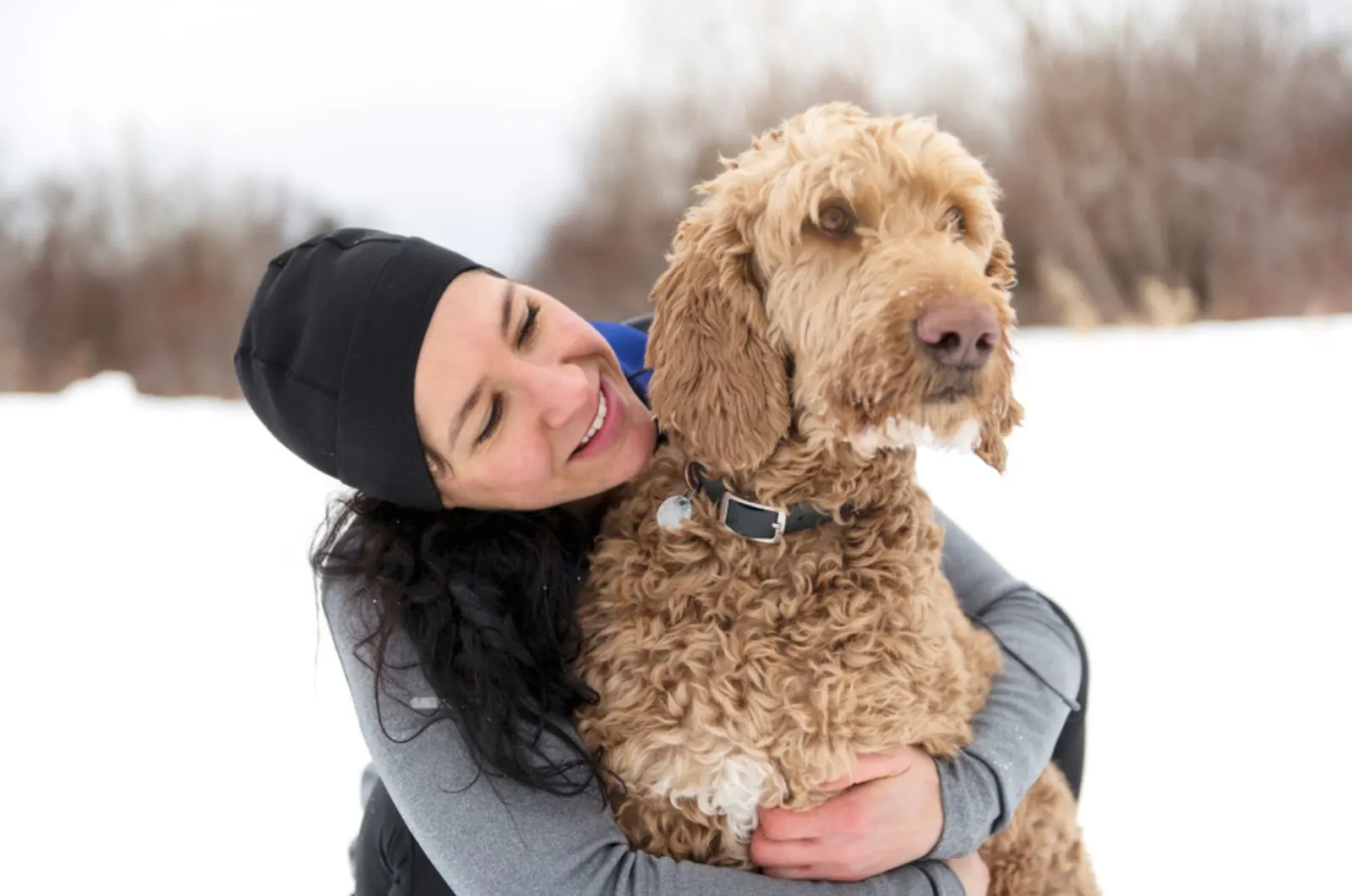 woman hugging goldendoodle on the snow