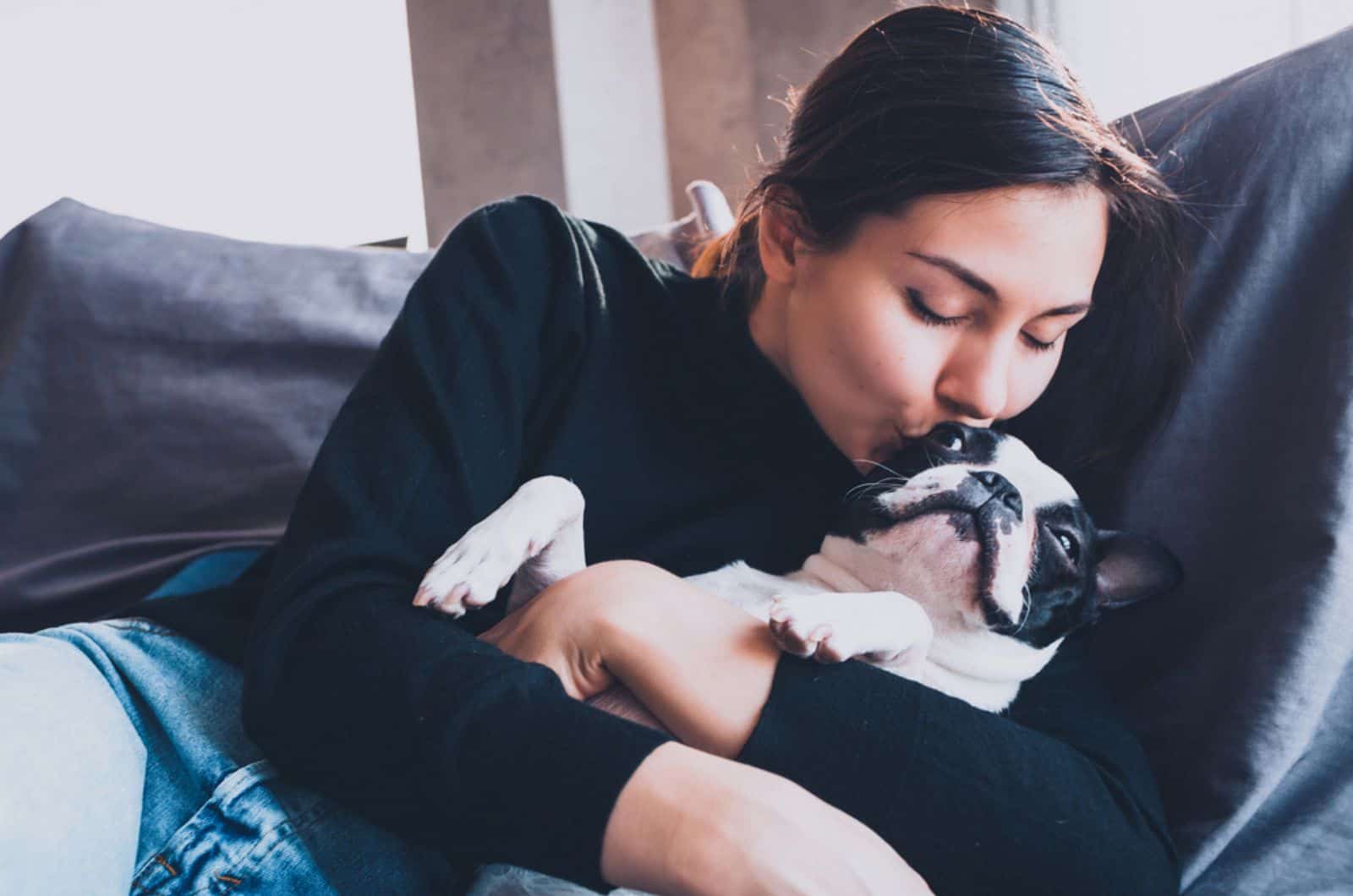 woman kissing her boston terrier dog on the couch