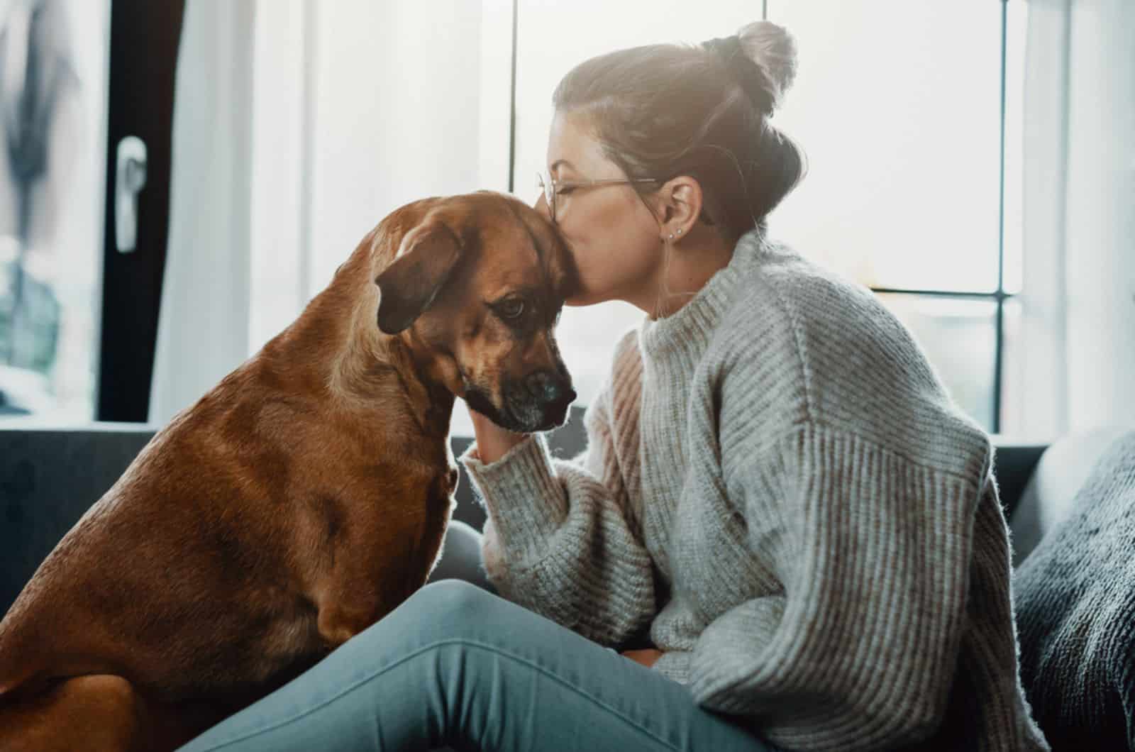 woman kissing her dog sitting close to her on the couch