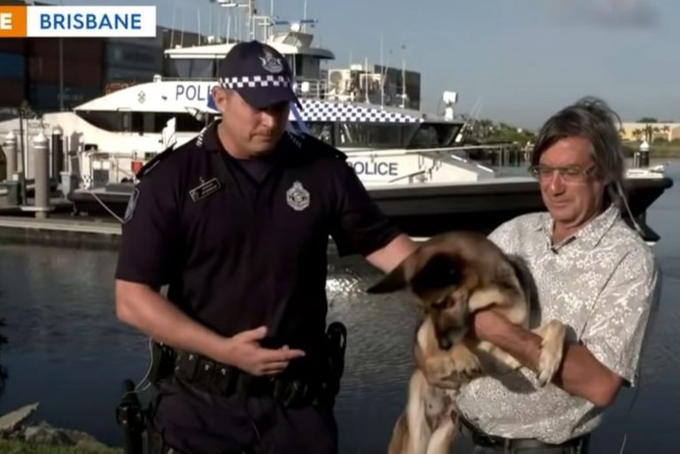 a man holds a dog in his arms while a policeman stands next to him