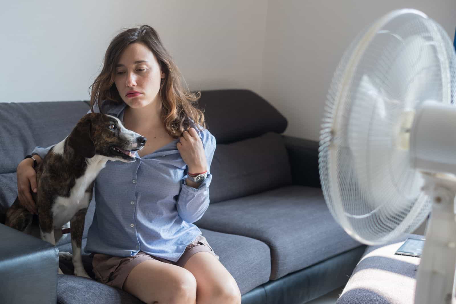 Young woman refreshing in front of cooling fan with her dog