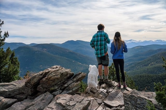 a man and a woman are standing on a rock with a dog