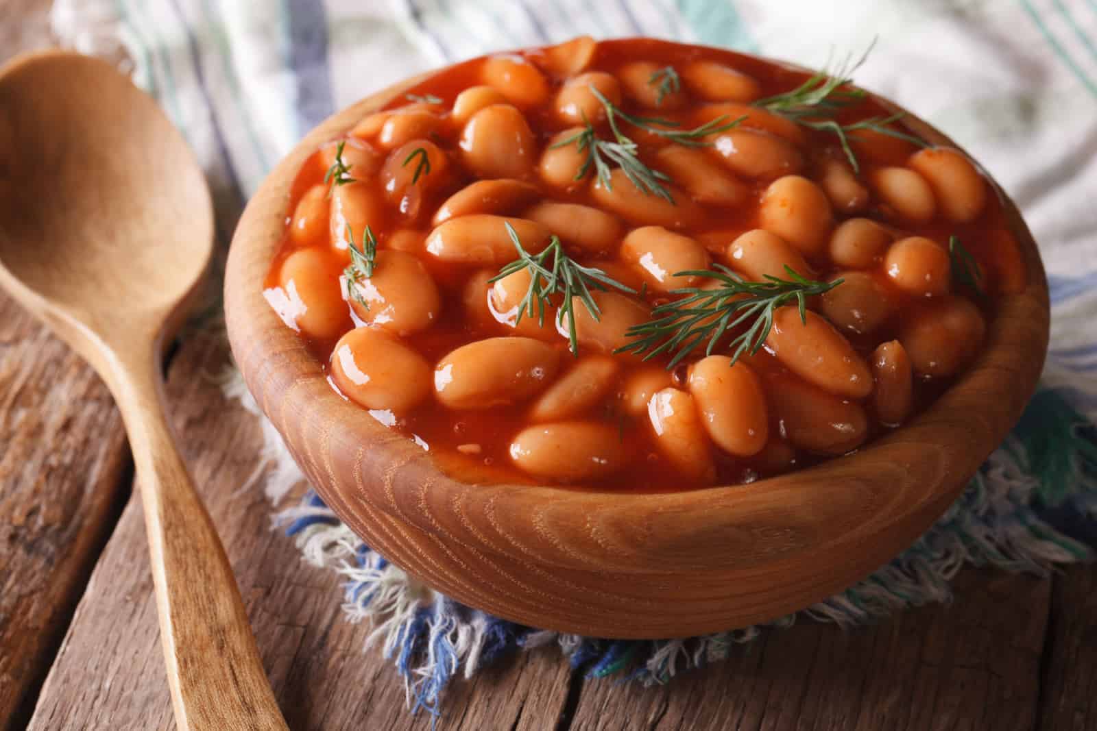 white beans in tomato sauce in a wooden bowl closeup