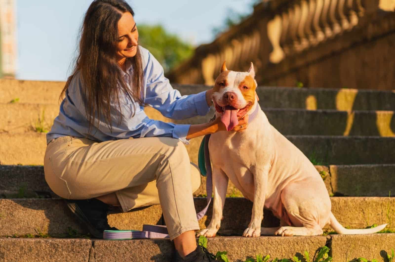 woman petting american pitbull terrier dog while sitting on stone stairs